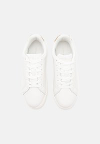 Vita sneakers med en slät läderöverdel, platta snören och en logotypdetalj vid hälen. Har en rund tå och en strukturerad sula.