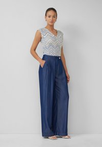Lichtgewicht, gestreepte top met een V-hals en korte mouwen. Wijde, donkere denimbroek met voorplooien en zijzakken.
