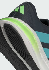 Chaussure de sport noire avec des rayures teal, accent vert sur la semelle, matériau texturé et semelle à motif pour une meilleure traction.