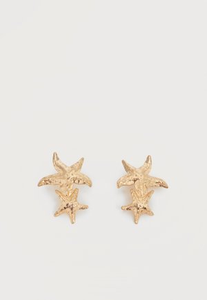Øreringe i guldfarve med to teksturerede søstjerneformer, en større og en mindre på hver ørering, mod en hvid baggrund.