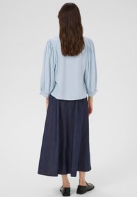 Blouse bleu clair avec des manches ballons, associée à une longue jupe en denim foncé. Chaussures noires visibles. Tissu lisse et coutures visibles.