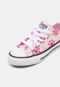 Tenisky Converse All Star s květinovým růžovým a bílým textilním svrškem, gumovým ochranným špičkovým krytem, bílými tkaničkami a černobílou pruhovanou podrážkou.
