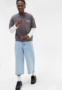 Szary t-shirt z krótkim rękawem nałożony na biały, długi rękaw, w połączeniu z jasnoniebieskimi spodniami o szerokich nogawkach i czarnymi butami.