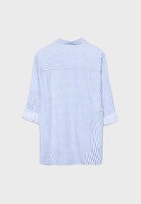 Camicia a maniche lunghe a righe azzurro chiaro e bianco con polsini arrotolati, vista da dietro su uno sfondo neutro.