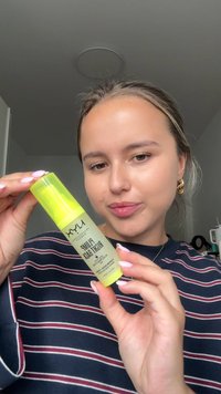 Flacon pommade vert avec un bouchon jaune transparent. L'étiquette comporte du texte en noir et blanc. La personne porte un haut rayé et tient le flacon.