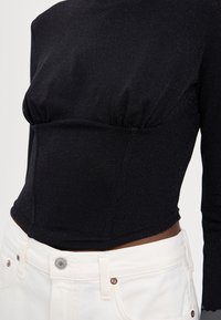 Zwarte longsleeve top met een textuurafwerking, met een geplooide buste en een getailleerde pasvorm, gecombineerd met witte high-waisted broek.
