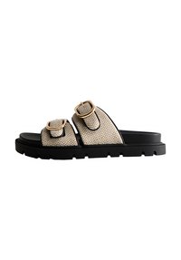 Beige vävda slidessandaler med två justerbara remmar, guldbucklor och en tjock svart gummisula med ett texturerat mönster.