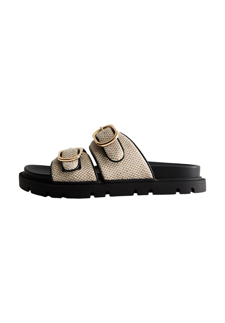 Beige vävda slidessandaler med två justerbara remmar, guldbucklor och en tjock svart gummisula med ett texturerat mönster.