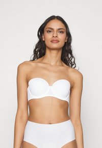 Hvit stroppeløs bh med glatte, formede kopper og sømløst design. Laget av stretchy, myk stoff, egnet for å bruke under ulike antrekk.