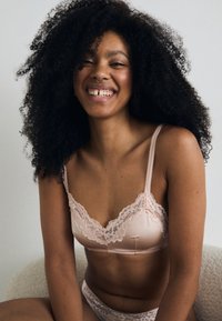 Bralette en dentelle rose clair avec bretelles ajustables et bordure en dentelle florale. Texture lisse, design délicat, bikini en dentelle assorti présenté.