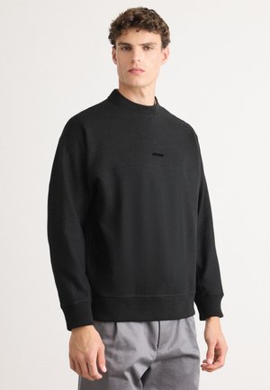 Svart sweatshirt gjord av mjukt material, med ribbad krage och mudd, med en matt logotyp på bröstet och en avslappnad passform.