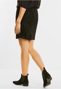 Falda negra texturizada con dobladillo en forma de ondas, con un patrón y combinada con botas de tobillo negras. La tela parece suave y tiene un diseño ajustado.