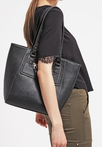 Svart faux läder tote-väska med dubbla handtag, strukturerad form, silverfärgade detaljer och en framficka. Texturerad yta med synlig sömnad.