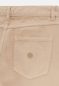 Tessuto di denim beige in primo piano con una tasca cucita decorata da un accento in metallo e una superficie testurizzata.