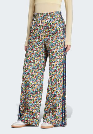 Femme portant un pantalon à jambes larges imprimé floral avec une ceinture élastique et des bandes latérales bleu marine, assorti à des baskets blanches et un haut beige.