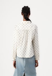 Vit långärmad blus med små svarta blommönster, plisserad ryggdetalj och knäppta manschetter. Matchad med en ljus denimkjol.