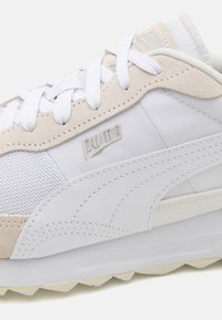 Baskets PUMA avec un schéma de couleurs blanc et beige clair, présentant des matériaux en maille et en daim, des lacets et une semelle en caoutchouc texturé.