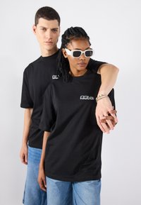 Mustad suurusega mustad T-särgid tekstikujundustega. Üks modell kannab valgeid prille. Hele sinine teksariie, sile kangas, ühtlane taust.