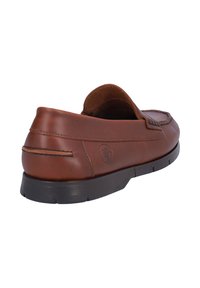 Zapato marrón de cuero sin cordones con un diseño redondeado, costuras contrastantes, una textura suave y una suela de goma con un detalle de logo.