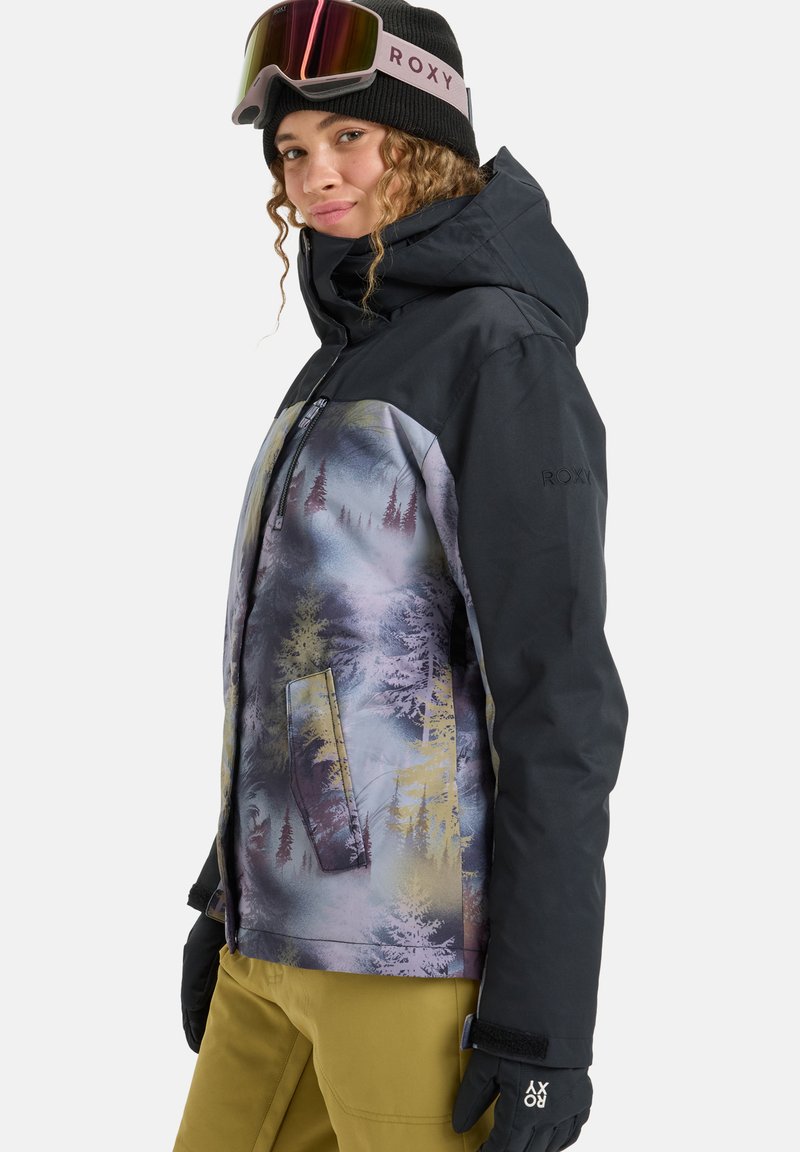 Multicolored ski jacket with a black upper, scenic pattern featuring trees, and two front pockets. Paired with black gloves and a beanie.