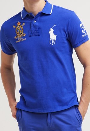 Polo-shirt bleu avec des bordures blanches, logo brodé et numéro 3 sur la poitrine. Manches courtes, en coton, avec un design en tissu texturé.