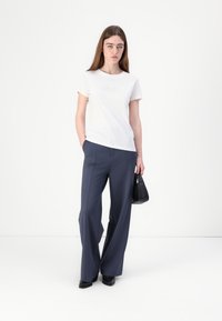 White cotton T-shirt with subtle embroidery, paired with high-waisted, wide-leg navy trousers. Model holding a small black handbag.