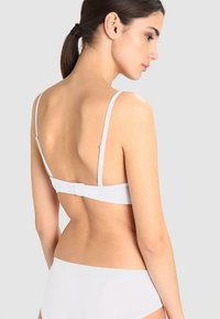Reggiseno bianco con spalline sottili, chiusure regolabili e una texture di tessuto liscia. Design semplice con una chiusura posteriore basica.
