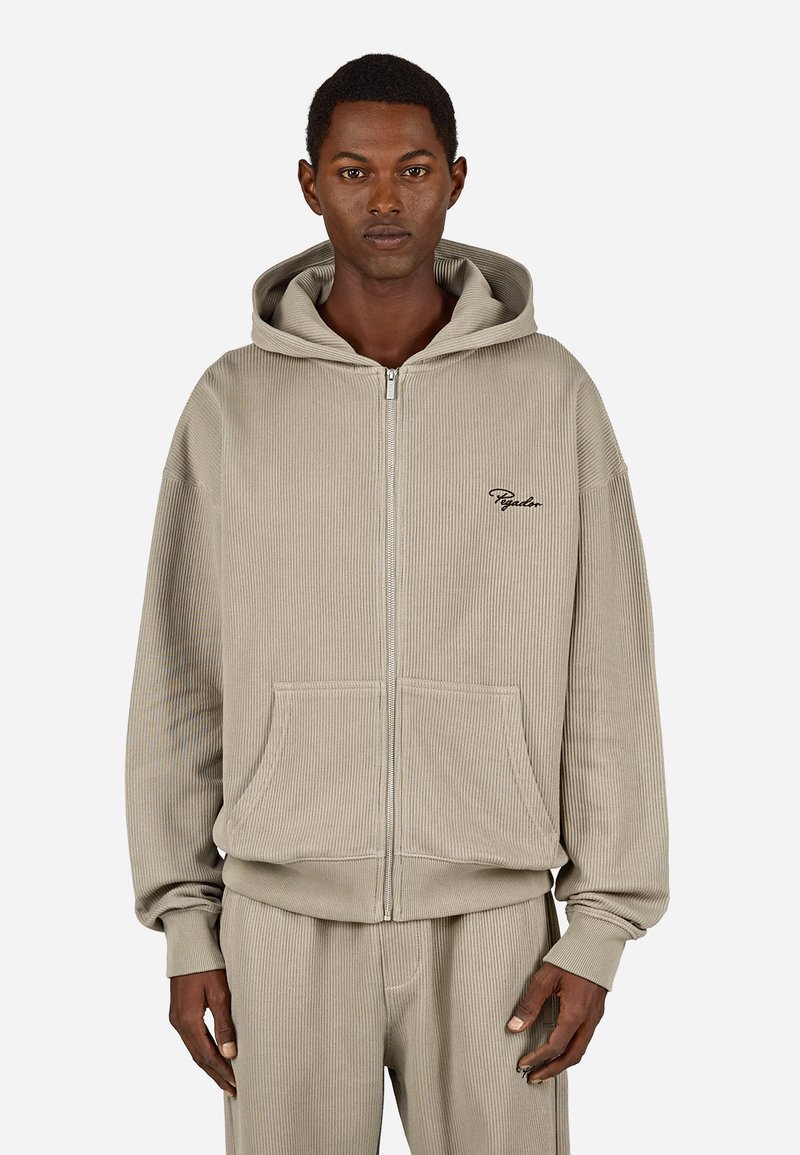 Beige glidlås hettegenser laget av ribbestrikket stoff, med en frontlomme, hette og subtil brodering på brystet. Myk tekstur og avslappet passform.