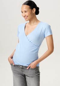Lys blå ribbet t-shirt med V-hals og korte ærmer, parret med grå jeans. T-shirten har en indpakket silhuet.