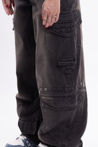 Los pantalones cargo de mezclilla negros holgados cuentan con múltiples bolsillos, un acabado texturizado y acentos metálicos. El diseño incluye costuras reforzadas.