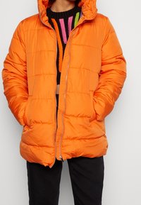 Chaqueta acolchada de color naranja brillante con capucha, cierre de cremallera y detalles de costura horizontal. Cuenta con dos bolsillos laterales y un corte relajado.