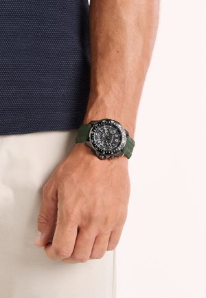 Schwarzes Zifferblatt mit grünem Silikonarmband, verfügt über mehrere Unterzifferblätter, auffällige Stundenmarkierungen und silberfarbene Akzente auf der Lünette.