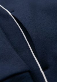 Zbliżenie na granatową tkaninę z białym cienkim paskiem na szwie lub fałdzie.