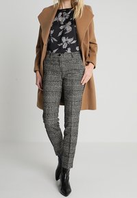 Brown wool coat over a black floral top, paired with gray plaid trousers and black ankle boots. The pattern features white lines.