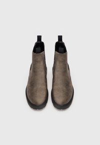 Een paar bruin leren Chelsea-boots met zwarte elastische zijpanelen en zwarte trekflappen, vanaf de voorkant weergegeven op een witte achtergrond.