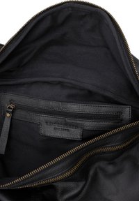 Interno di una borsa in pelle nera con una texture liscia, dotata di una tasca con zip, etichetta con la scritta "RE:DESIGNED" e hardware della cerniera in tono oro.