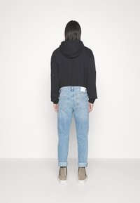Zwarte cropped hoodie met een capuchon, gecombineerd met lichtblauwe jeans met opgerolde manchetten en grijze enkellaarsjes met witte zolen. Eenvoudig en modern ontwerp.