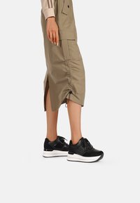 Sneaker nere con finitura testurizzata, suola piatta bianca e lacci. Abbinate a una gonna beige al ginocchio con spacchi laterali.