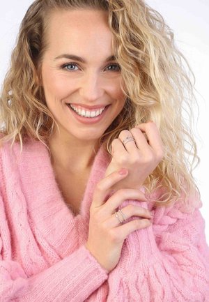 Pink knitted sweater with a V-neck, featuring a fuzzy texture. Model shows three silver rings on the left hand, with a warm smile.