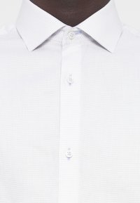 Weißes Hemd mit Knöpfen, das ein strukturiertes kariertes Muster, einen klassischen Kragen und kontrastierende weiße Knöpfe aufweist.