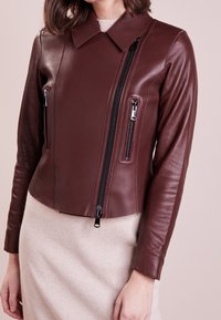 Burgunderfarbene Leder-Croppjacke mit einem Kragenhals, zwei vorderen Reißverschlusstaschen und einem zentralen Reißverschluss. Glatte Textur, taillierte Passform.