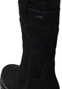 Musta mokkanahka saapas, jossa on teksturoitu neulekaulus, sivussa nappi ja kontrastisaumat. Kestävä kumipohja.