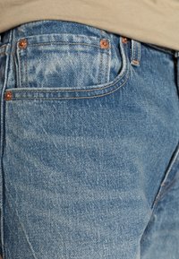 Světle modré džíny z denimu s klasickým pětikapsovým designem, viditelnou měděnou kovovou částí a kontrastním šitím na pasu.