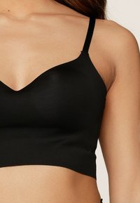 Bralette nera con una superficie liscia, scollo profondo e sottili spalline regolabili, progettato per comfort e supporto.