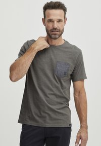 Šedé tričko s kulatým výstřihem, krátkými rukávy a kontrastní kapsou z denimu. Má měkkou texturu a volný střih.