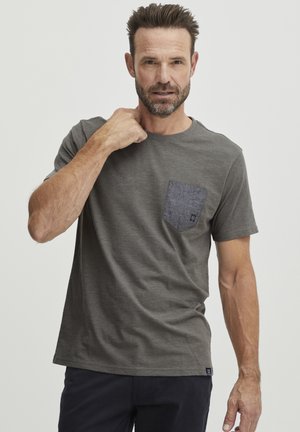 Camiseta gris con cuello redondo, mangas cortas y un bolsillo de parche de mezclilla en contraste. Presenta una textura suave y un corte relajado.
