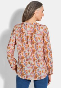 Langemouwige top van lichte stof, met een multikleurig bloemenpatroon in roze, oranje en paars. Ronde onderkant en knopenmanchetten.