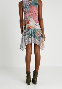 Kleid mit Blumenmuster und asymmetrischem Saum, aus leichtem Stoff gefertigt. Es hat eine Spitzenverzierung und lebendige Farben, darunter Pink und Grün.