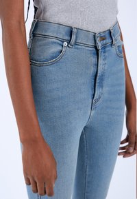 High-waisted blue denim jeans with a slim fit, featuring front pockets, belt loops, and light stitching accents on the seams.