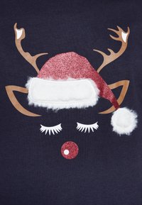 Maglietta blu navy con disegno di una faccia di renna con naso rosso scintillante, cappello bianco soffice e corna marroni. Include dettagli bianchi come ciglia.